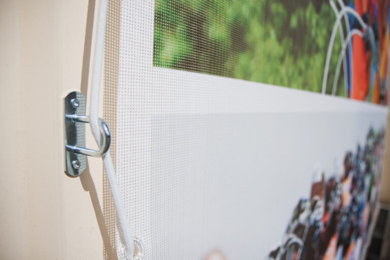 Gros plan sur une attche d'une banderole microperforée avec sandow blanc - Next publicité Vosges